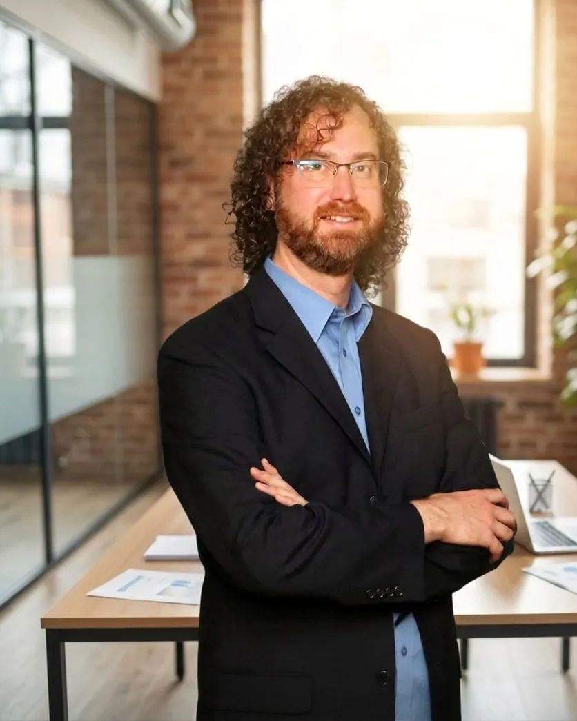Matt Ray Smith in a dark blazer, arms folded, in an office
